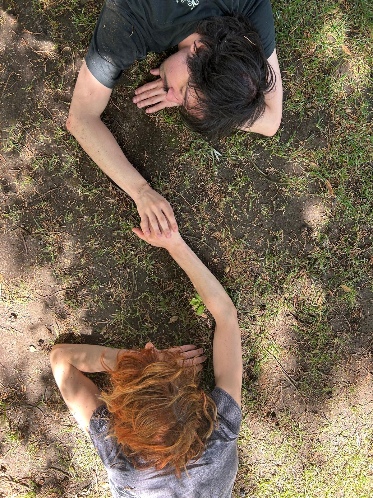 Two people lying on the ground, hands reaching to meet